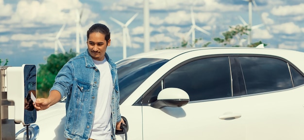 Homme progressiste avec sa voiture EV et éolienne comme concept d'énergie renouvelable