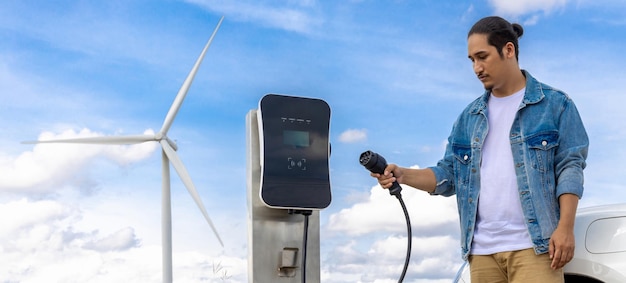 Homme progressiste avec sa voiture EV et éolienne comme concept d'énergie renouvelable