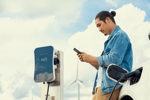 Homme progressiste avec sa voiture EV et éolienne comme concept d'énergie renouvelable