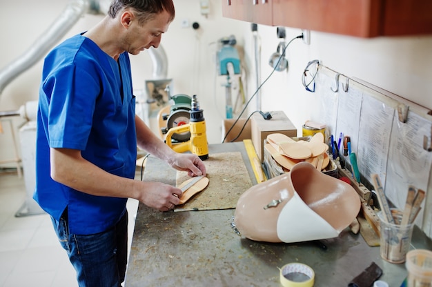 Homme prothésiste faisant des semelles orthopédiques tout en travaillant en laboratoire.