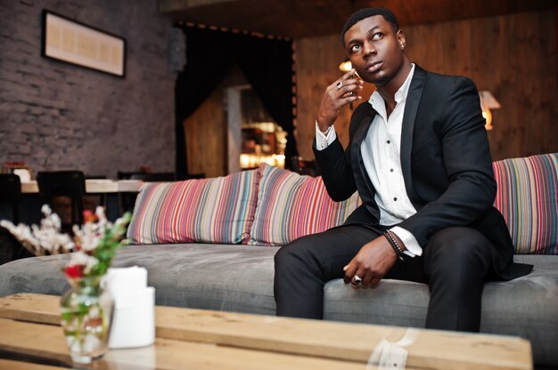 Homme puissant et fort en costume noir assis sur le canapé et parle au téléphone à l'intérieur