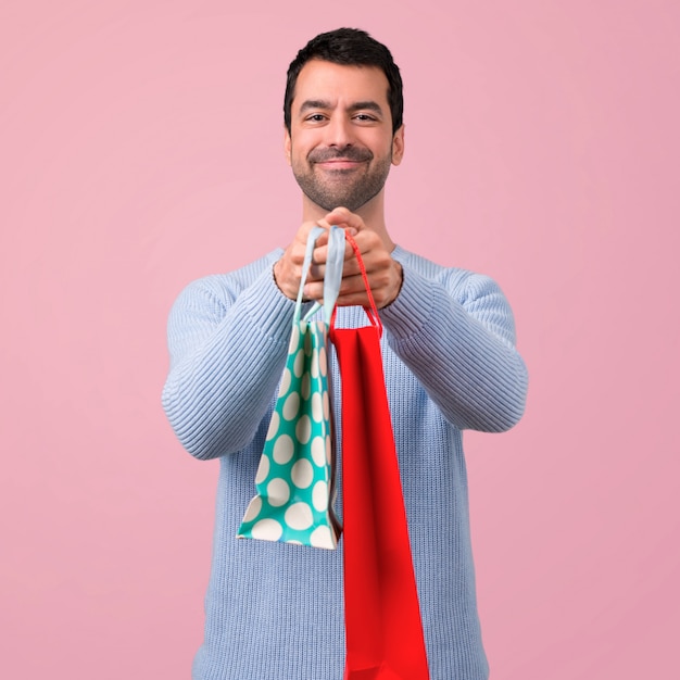 Homme avec un pull bleu tenant beaucoup de sacs à provisions