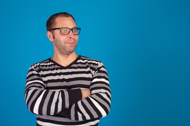 L'homme en pull et avec des lunettes sourit sur fond bleu