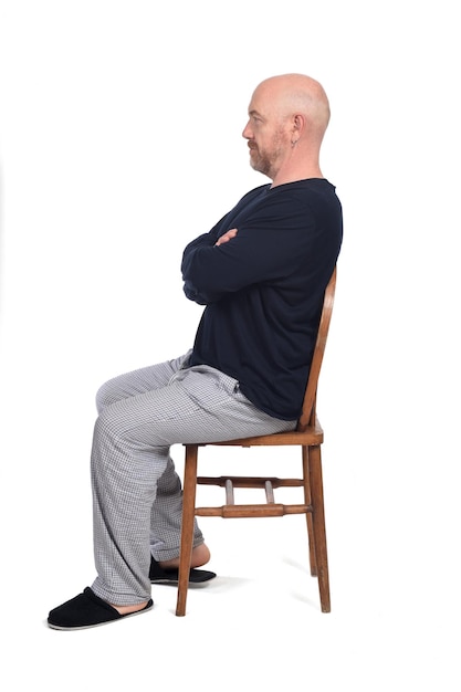 Homme en pyjama assis sur une chaise sur fond blanc, vue latérale et bras croisés