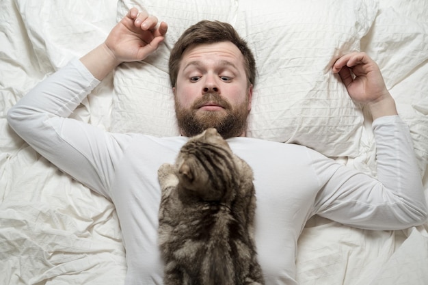 Photo un homme en pyjama blanc a été réveillé par un chat bien-aimé qui dormait sur la poitrine qu'il a surpris