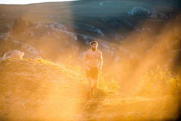 Un homme qui court sur une montagne au petit matin alors que le soleil se lève.