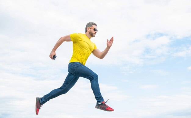 Homme qui court avec un smartphone sur fond de ciel