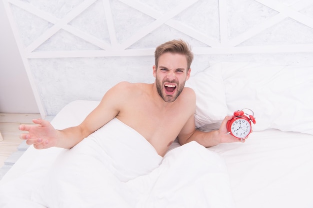 Homme qui dort lit draps blancs et réveil rouge se sentant irrité concept