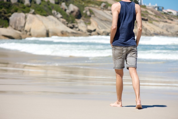 Homme qui marche pieds nus sur la plage de sable blanc