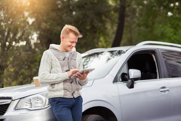 Homme qui réussit à l'aide d'une tablette numérique tout en se tenant près de sa voiture à l'extérieur.