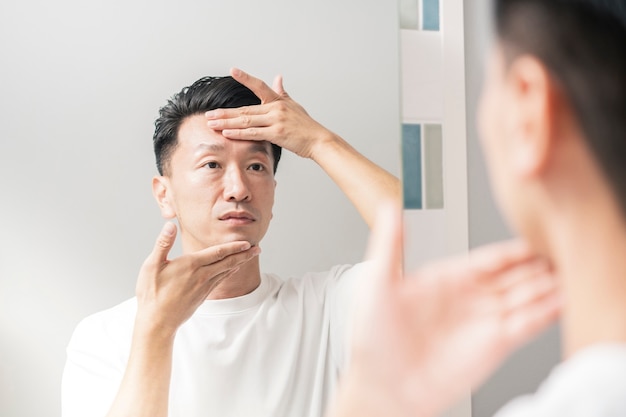 Un homme qui se regarde dans le miroir et vérifie l'état de sa peau