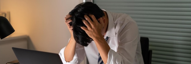 L'homme qui travaille au bureau ce soir se tient la tête parce qu'il est stressé par le travail