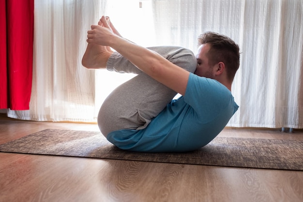 Homme de race blanche à Apanasana ou Wind pose à la maison