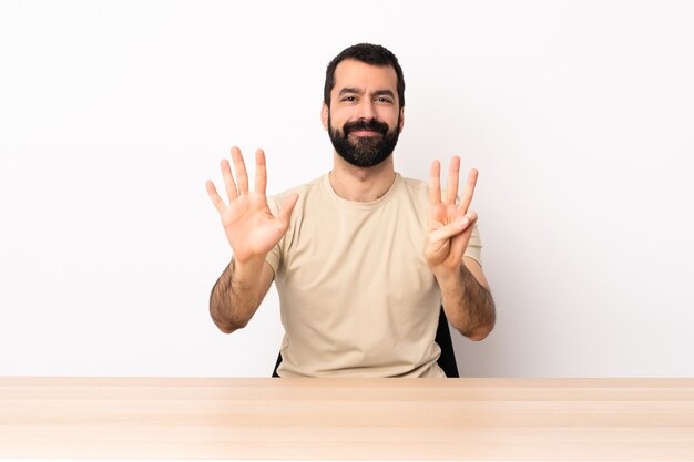 Homme de race blanche avec barbe dans une table comptant huit avec les doigts.