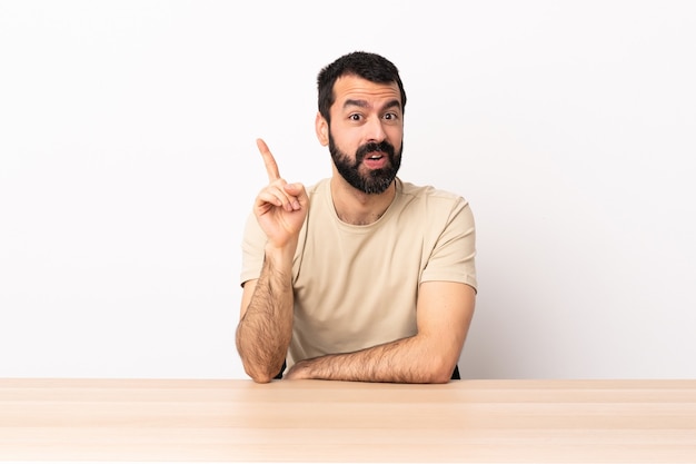 Homme de race blanche avec barbe dans une table dans l'intention de réaliser la solution tout en levant un doigt.