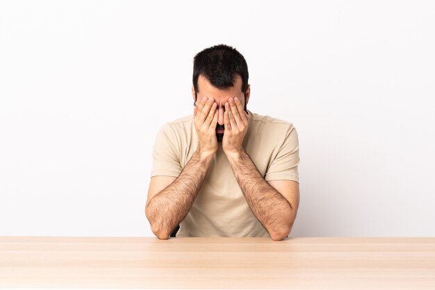 Homme de race blanche avec barbe dans une table avec une expression fatiguée et malade.