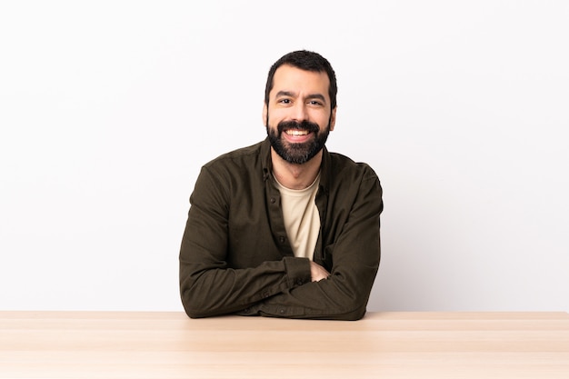 Homme de race blanche avec barbe dans une table en gardant les bras croisés en position frontale