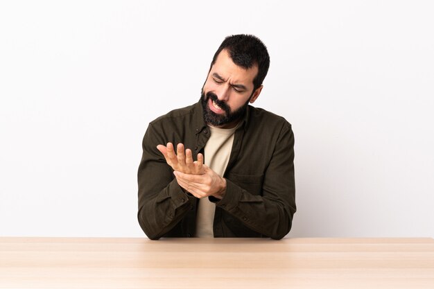 Homme de race blanche avec barbe dans une table souffrant de douleurs dans les mains