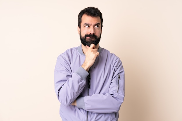 Homme de race blanche avec barbe portant une veste sur fond isolé ayant des doutes et de la pensée