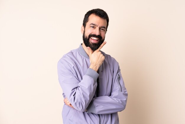 Homme de race blanche avec barbe portant une veste sur le mur heureux et souriant