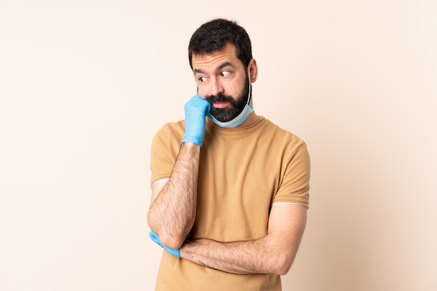 Homme de race blanche avec barbe protégeant avec un masque et des gants sur le mur avec une expression fatiguée et ennuyée