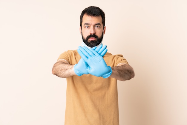 Homme de race blanche avec barbe protégeant avec un masque et des gants sur le mur faisant un geste d'arrêt avec sa main