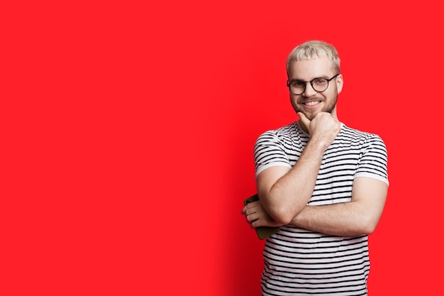 Homme de race blanche blonde avec des lunettes posant sur un fond rouge avec un espace libre touchant le menton et regardant à l'avant