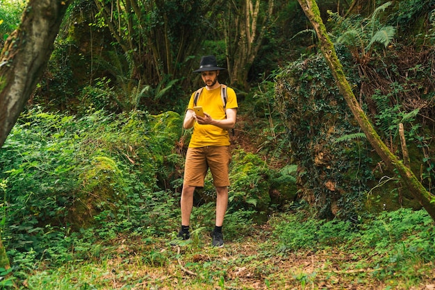 Homme de race blanche dans un t-shirt jaune tapant avec son téléphone intelligent dans la jungle par une journée ensoleillée