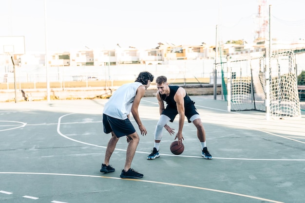 Homme de race blanche dribble un ami dans un match de basket-ball dans un tribunal urbain à l'extérieur