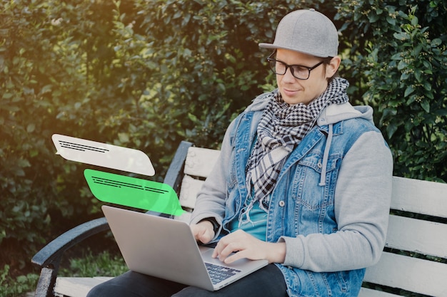 Un homme de race blanche est assis sur un banc et communique sur les messageries instantanées et les réseaux sociaux