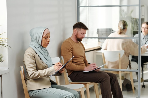 Homme de race blanche et femme musulmane en hijab assis sur des chaises à l'ambassade ou à l'agence de service des visas