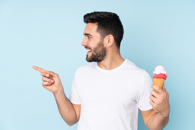 Homme de race blanche avec une glace au cornet sur mur bleu pointant vers le côté pour présenter un produit