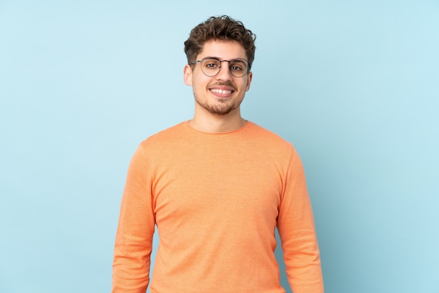 Homme de race blanche isolé sur mur bleu avec des lunettes et heureux