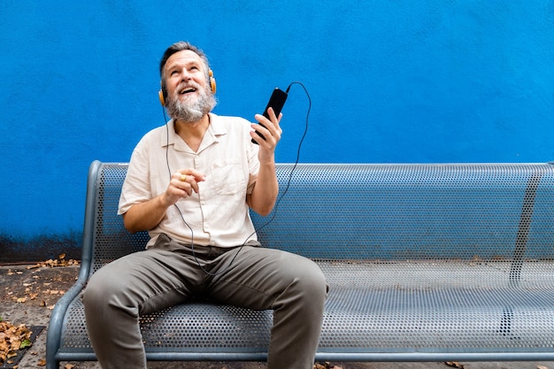 Homme de race blanche mature adulte appréciant la musique à l'extérieur à l'aide d'un téléphone portable et d'un casque. Espace de copie. Mode de vie.