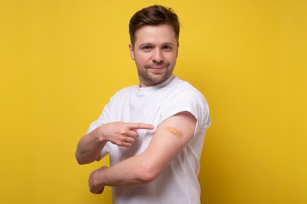 Homme de race blanche montrant son bras vacciné Il a reçu un vaccin corona en regardant la caméra Studio tourné sur un mur jaune