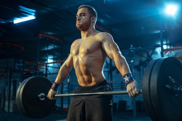 Homme de race blanche pratiquant l'haltérophilie dans la salle de gym. Entraînement de modèle sportif masculin caucasien avec haltères, semble confiant et fort. Musculation, mode de vie sain, mouvement, activité, concept d'action.