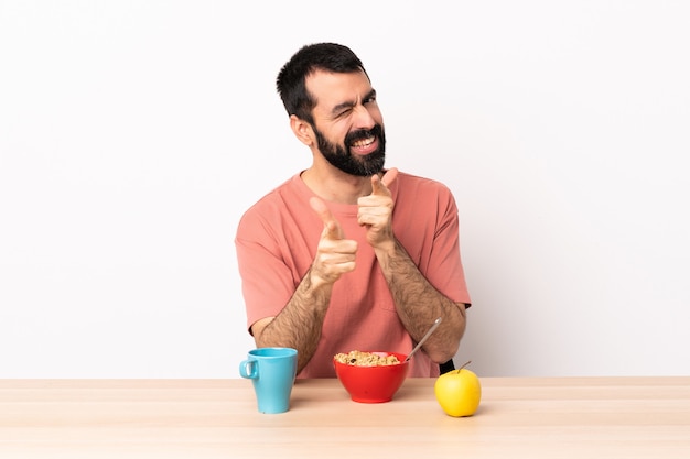 Homme de race blanche prenant son petit déjeuner dans une table pointant vers l'avant et souriant