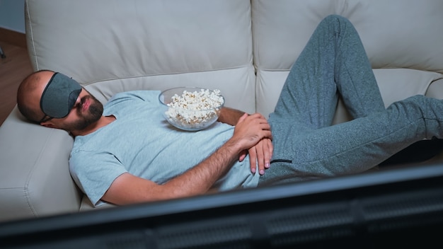 Homme de race blanche s'endormir en regardant un film assis sur un canapé