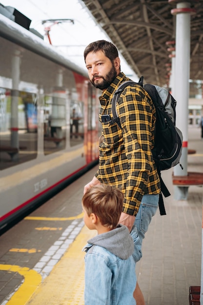 Homme de race blanche avec sac à dos tenant un petit fils à la main debout sur la plate-forme pour prendre le train