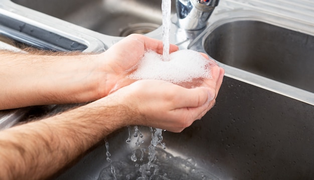 Un Homme De Race Blanche Se Lave Les Mains Dans Un évier En Métal Avec Du Savon. Concept De Soins De Santé D'hygiène Et De Désinfection Des Mains.