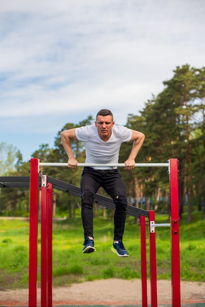 Un homme de race blanche se tire sur une barre horizontale sur un terrain de sport