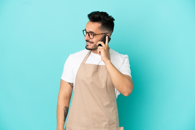 Homme de race blanche de serveur de restaurant d'isolement sur le fond bleu gardant une conversation avec le téléphone portable avec quelqu'un