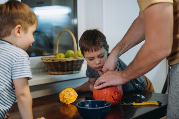 Homme de race blanche avec ses fils mignons dessinant les yeux sur une citrouille pour faire une lanterne Jack traditionnelle. photo de haute qualité