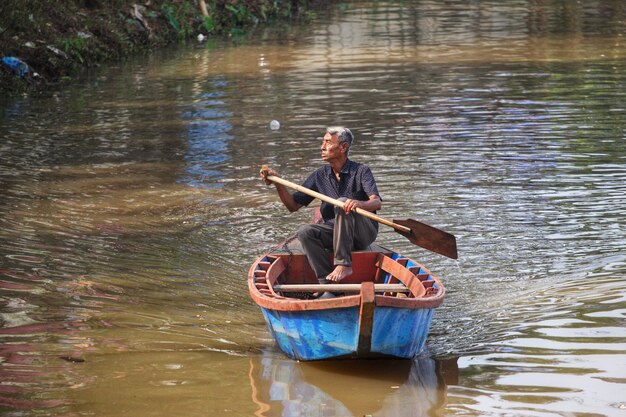 Un homme rame un bateau avec un bâton.