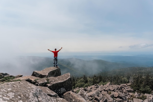 L'homme de randonneur sur le dessus de la montagne apprécie la vue aérienne soulevant ses mains au-dessus des nuages Mont Pidan