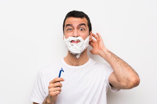 Homme rasant sa barbe sur un mur blanc isolé ayant des doutes