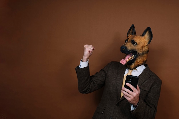 Un homme ravi avec smartphone et un masque de tête de chien en latex levant les mains