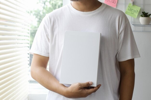 Homme recadré tenant un livre sur la poitrine pour une maquette de livre