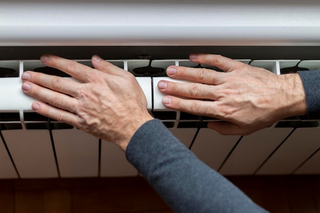 Un homme réchauffe ses mains sur un radiateur de chauffage près d'un gros plan du mur blanc