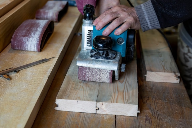 Un homme rectifie des planches avec une ponceuse